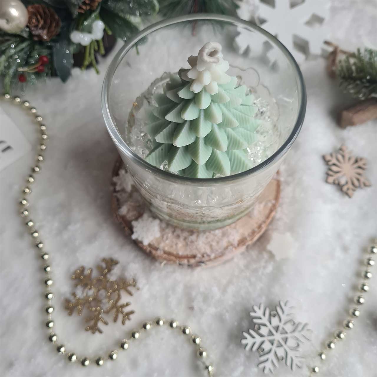 Handgegossene Weihnachtskerze mit Tannenbaum auf winterlichem Hintergrund